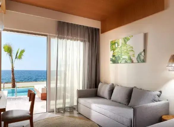 Sofa in einem hellen Hotelzimmer mit Blick durch die Glasfront auf Terrasse und Meer.