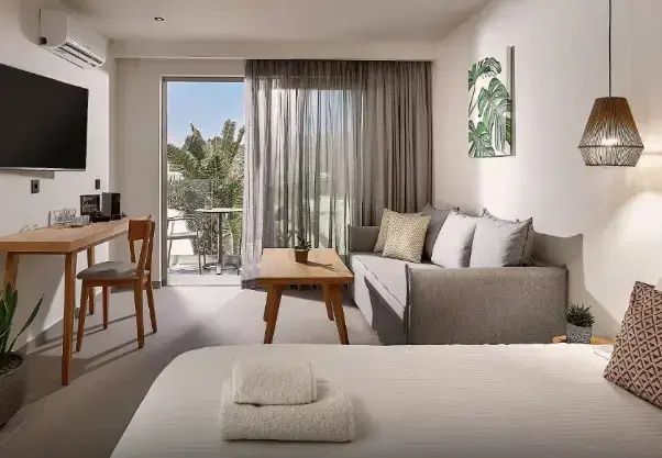 Wohnbereich eines Hotelzimmers mit Sofa, Holztisch und Blick auf den Balkon.