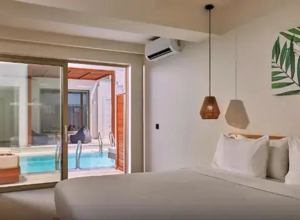 Helles Hotelzimmer mit großem Bett, Hängelampe und direktem Zugang zum Poolbereich.