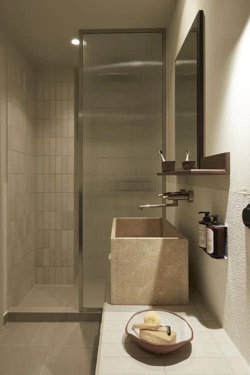 Badezimmer mit einem eckigen Waschbecken aus Stein und einer Dusche hinter Glas.