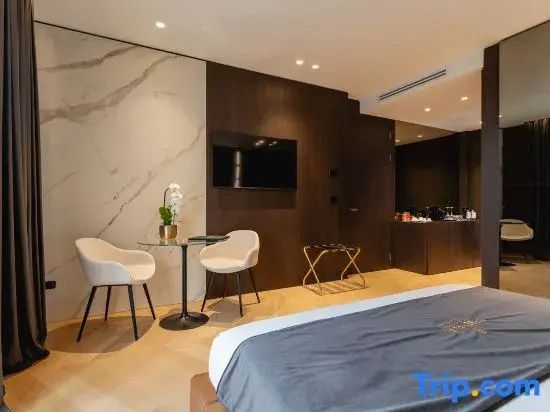 Schlafbereich der Suite mit Doppelbett, Flachbild-TV an dunkler Holzwand und Sitzgruppe.