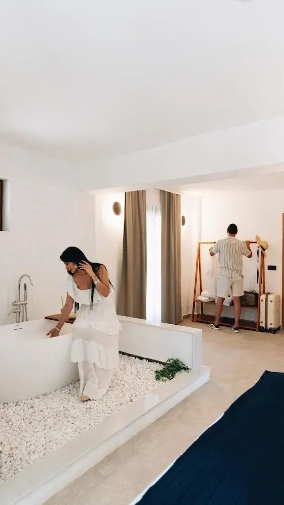Offenes Hotelzimmer mit freistehender Badewanne und Garderobenständer im Hintergrund.