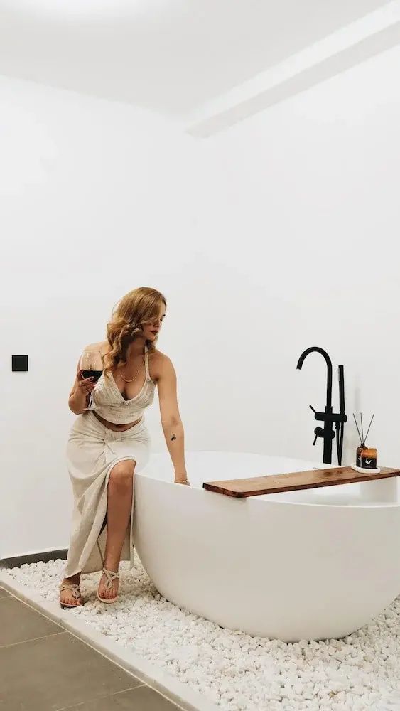 Freistehende weiße Badewanne mit schwarzer Armatur und Holzablage an einer weißen Wand.