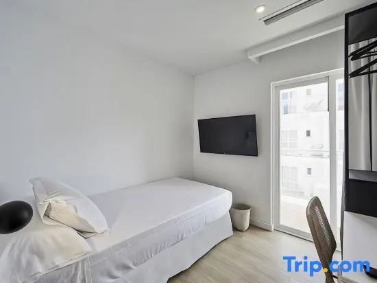 Helles Hotelzimmer mit weiß bezogenem Bett, Wand-TV und Zugang zum Balkon.