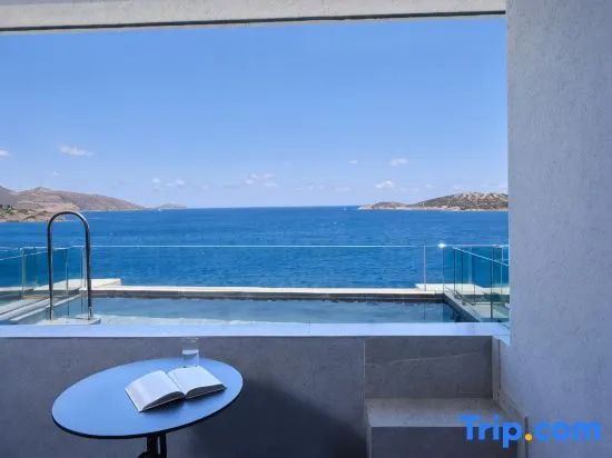 Blick von einer Terrasse mit Tisch und Buch über einen Pool auf das blaue Meer.