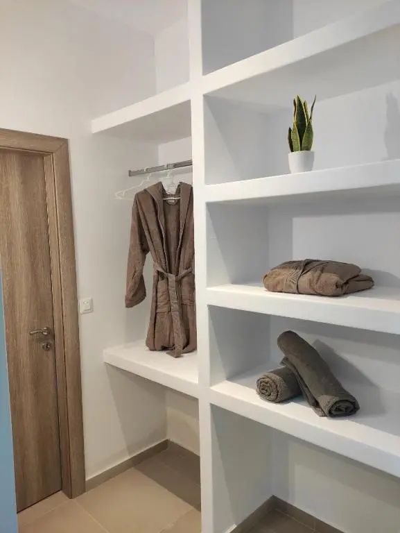 Weißes Wandregal mit zusammengelegten Handtüchern, Bademantel und einer kleinen Pflanze.