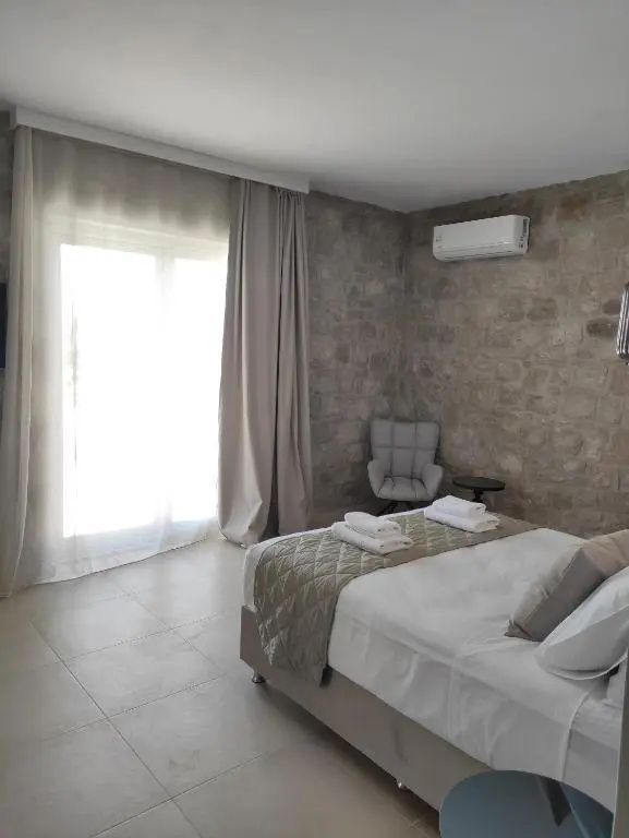 Heller Schlafraum mit Natursteinwand, Sessel und bodentiefem Fenster mit Vorhängen.