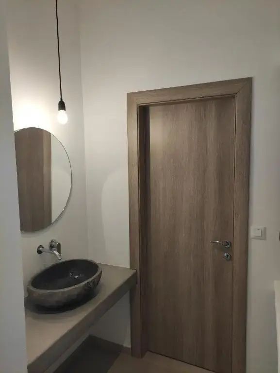 Ovales Steinwaschbecken mit rundem Spiegel, Hängelampe und einer Holztür.