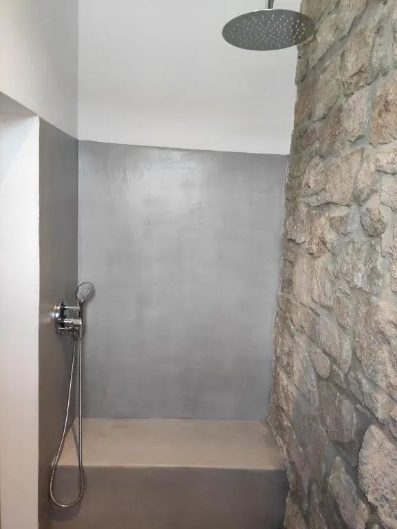 Dusche mit grauen Putzwänden, einer Handbrause und einer Wand aus natürlichem Naturstein.
