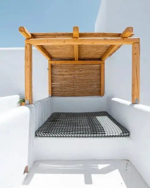 Überdachter Liegebereich aus Holz auf einer weiß getünchten Terrasse.