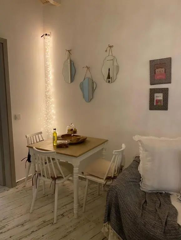 Kleiner Holztisch mit weißen Stühlen, Wandspiegeln und einer Lichterkette im Wohnbereich.