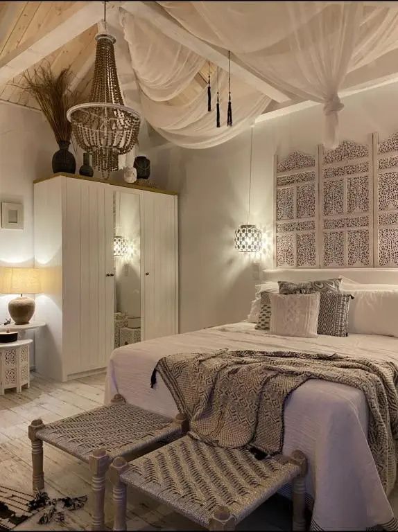 Bett im Boho Stil mit hellen Textilien, Holzschrank und verziertem Kopfteil aus Holz.