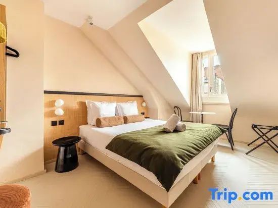 Helles Hotelzimmer im Dachgeschoss mit Doppelbett, grüner Tagesdecke und Fenster.