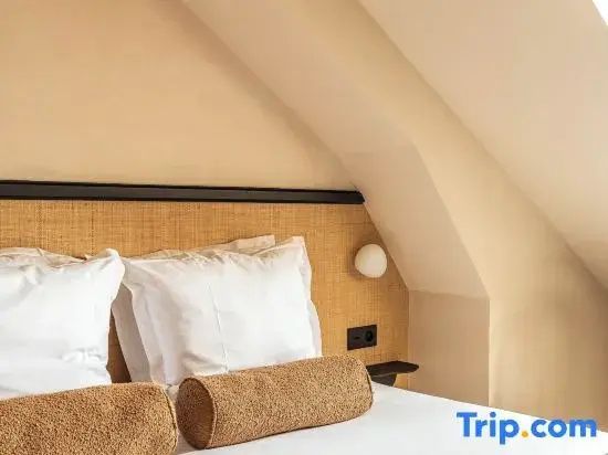 Doppelbett mit weißen Kissen, brauner Nackenrolle und Kopfteil aus Geflecht unter einer Dachschräge.