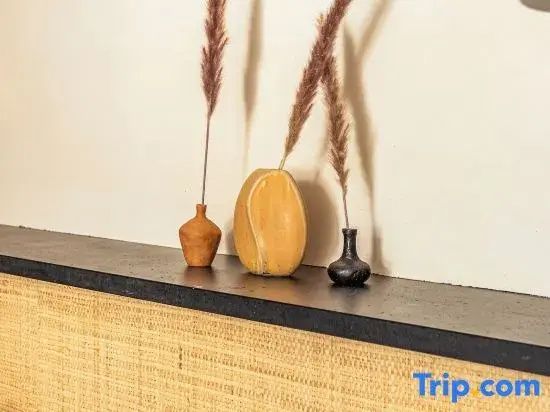 Drei kleine Tonvasen mit getrocknetem Ziergras auf einer dunklen Ablage vor einer beigen Wand.
