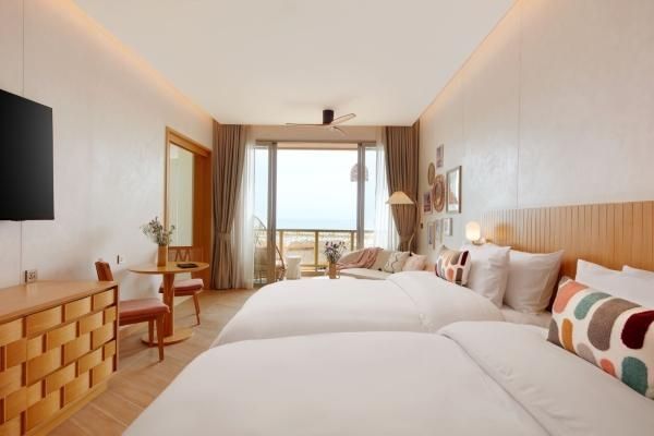 Helles Hotelzimmer mit zwei Betten, Sitzbereich und Zugang zum Balkon.