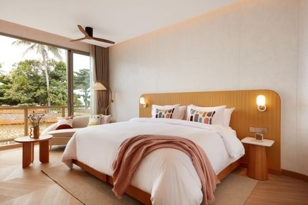 Helles Hotelzimmer mit großem Doppelbett, Deckenventilator und Sitzcouch am Fenster.