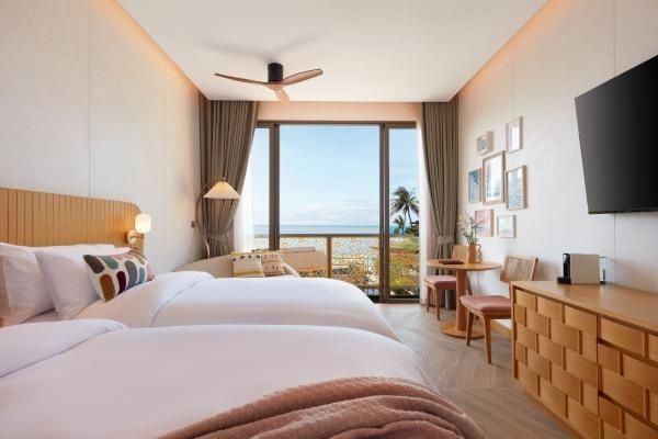 Blick aus dem Hotelzimmer durch die Glasfront auf den Balkon, Palmen und das Meer.