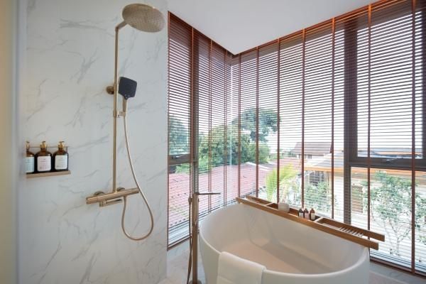 Badezimmer mit freistehender Wanne, Regendusche und großen Fensterfronten.
