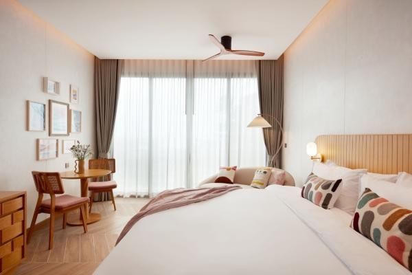 Hotelzimmer mit Sitzbereich am Fenster, Holzstühlen und verhangener Glasfront.