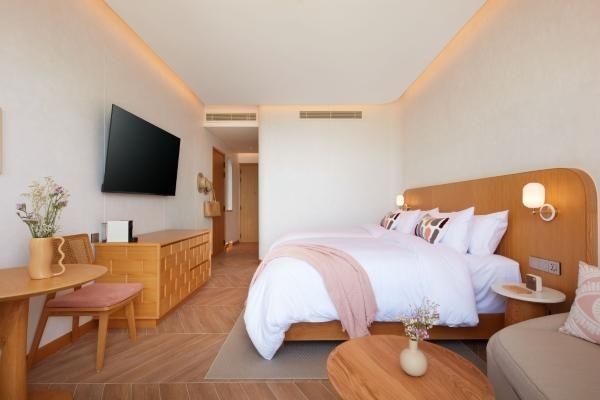 Helles Schlafzimmer mit Holzmöbeln, Wandfernseher und zwei zusammenstehenden Betten.
