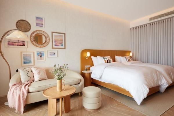 Helles Hotelzimmer mit Holzkopfteil, zwei Einzelbetten, Sofa und kleiner Bilderwand.