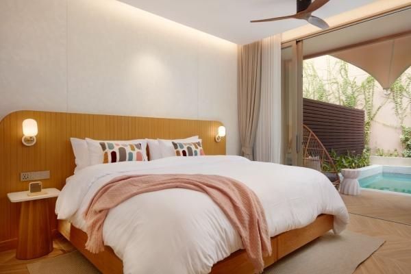 Doppelbett mit Holz-Kopfteil, rosa Tagesdecke und Tür zum angrenzenden Außenbereich.