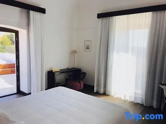 Helles Hotelzimmer mit weiß bezogenem Bett, Schreibtisch und bodentiefen Fenstern.