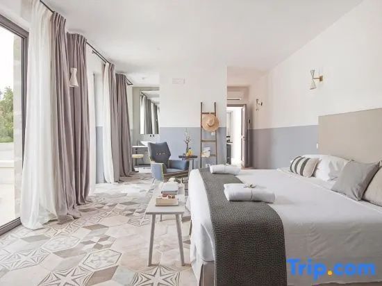Hell eingerichtetes Hotelzimmer mit Doppelbett, gemustertem Fliesenboden, Sessel und langen Vorhängen.