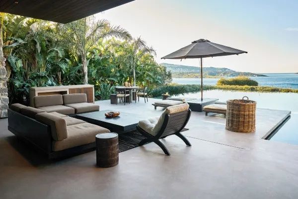 Terrasse mit Loungemöbeln, Sonnenschirm und Blick auf den Pool sowie das Meer.