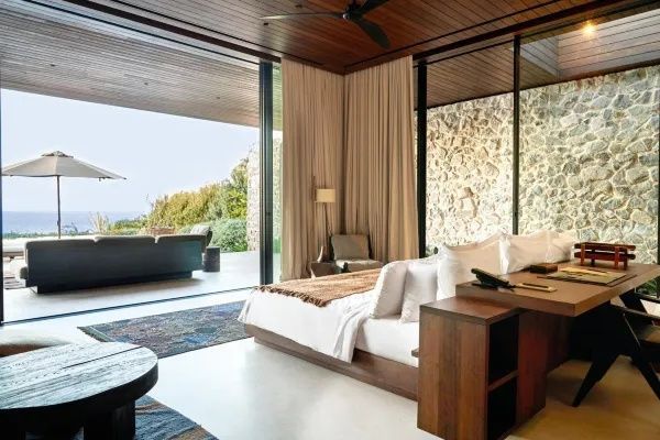 Schlafbereich einer Suite mit großem Doppelbett und geöffneter Glasfront zur Terrasse.