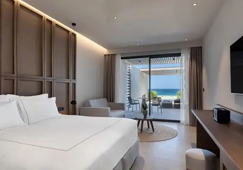 Hotelzimmer mit Doppelbett und Sitzecke sowie Blick über die Terrasse auf das Meer.