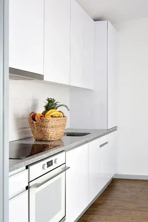 Moderne weiße Küchenzeile mit Induktionskochfeld, Spüle und grauem Arbeitsplattendesign.
