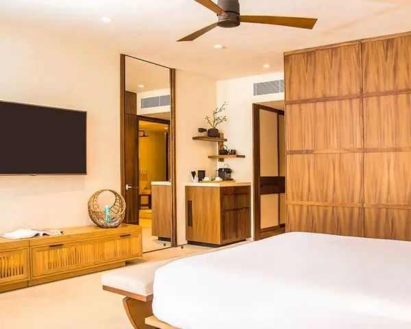 Schlafbereich mit Fernseher, Minibar-Ecke, Holzschrank und Blick in das Badezimmer.