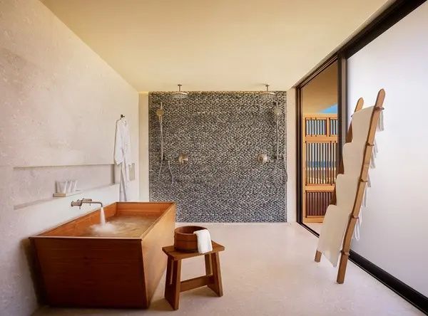 Badezimmer mit hölzerner Badewanne, Regenduschen an einer Steinwand und Holzschemel.