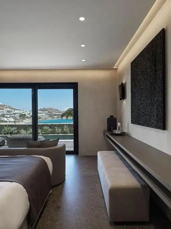 Modernes Hotelzimmer mit Doppelbett, Wandkonsole und Blick auf das Meer durch große Fensterfront.