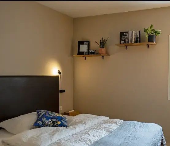 Doppelbett mit weißer Bettwäsche, dunkelblauem Kissen und Wandregalen mit Dekoration.