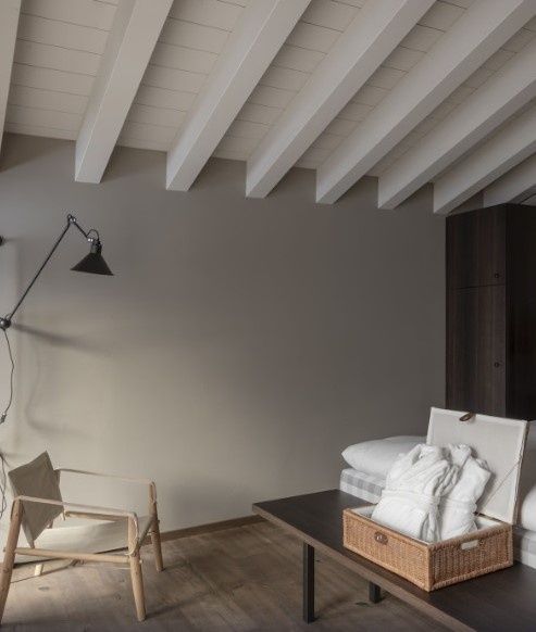 Hotelzimmer mit hellen Holzdeckenbalken, einem Holzstuhl und einem Korb mit Bademänteln.