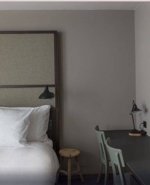 Blick in die Ecke eines Hotelzimmers mit Bett, Holzschemel und Schreibtisch mit Stühlen.