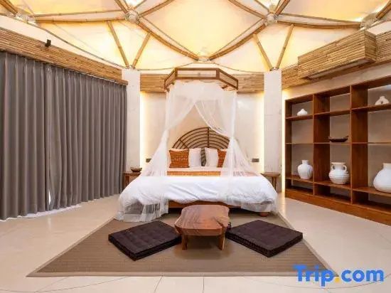 Schlafbereich mit Himmelbett, Moskitonetzen, Bambusdecke und einem offenen Holzregal mit Tonvasen.