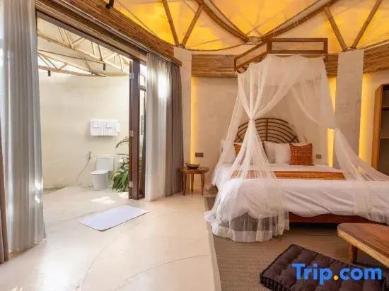 Helles Hotelzimmer mit Moskitonetzen am Bett und geöffneter Tür zum angrenzenden Sanitärbereich.