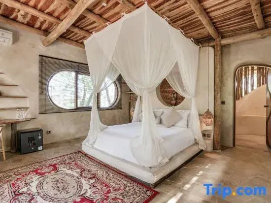 Schlafzimmer mit einem Himmelbett, weißem Moskitonetz, Holzdecke und ovalem Fenster