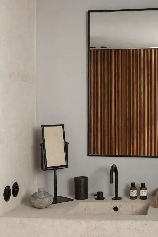 Waschtisch mit schwarzer Armatur, Kosmetikspiegel und Holzlamellenwand im Hintergrund.