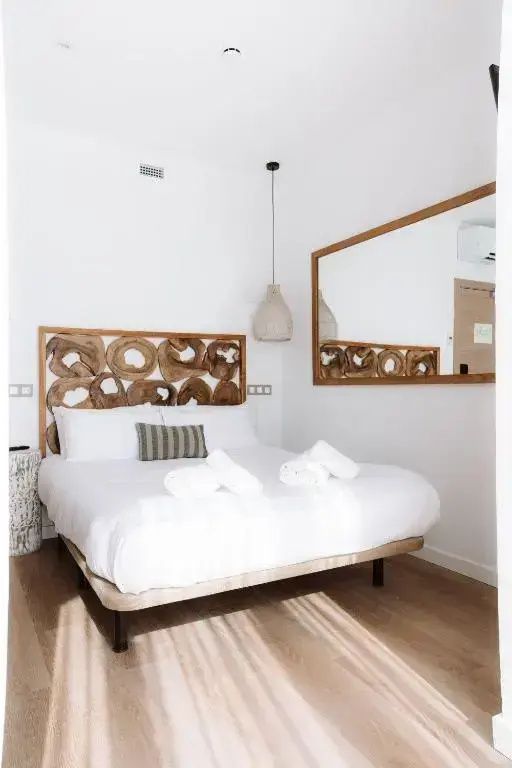 Doppelbett mit einem Kopfteil aus Holzscheiben und weißer Bettwäsche.