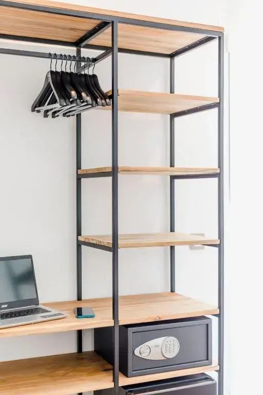 Offenes Regal aus schwarzem Metall und Holz mit Kleiderbügeln und integrierter Arbeitsfläche.