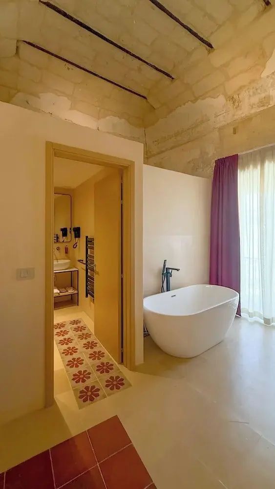 Freistehende weiße Badewanne im Zimmer neben der Tür zum Badezimmer mit Fliesen.