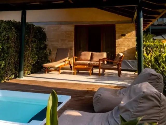 Überdachte Terrasse mit Holzmöbeln, Sonnenliege und Sitzsack am Rand eines Pools.