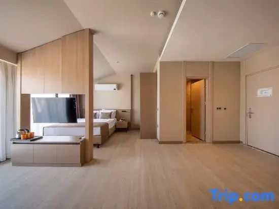 Weitläufiges Hotelzimmer mit Holzboden, Raumteiler, Bettbereich und offener Tür.