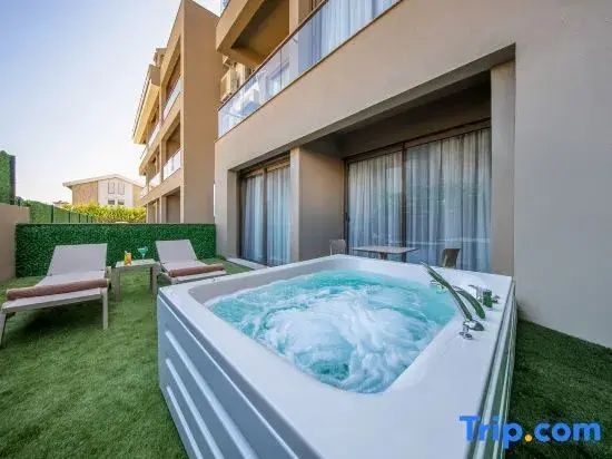 Terrasse im Außenbereich mit Whirlpool, Sonnenliegen und Kunstrasen vor der Fassade.