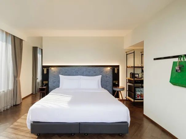 Helles Hotelzimmer mit bezogenem Doppelbett, blauem Kopfteil und offenem Kleiderschrank.